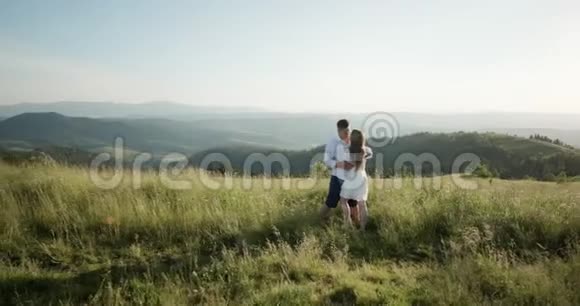 年轻可爱的情侣拥抱亲吻对方在绿色茂密的山区夏天日落两个目标视频的预览图