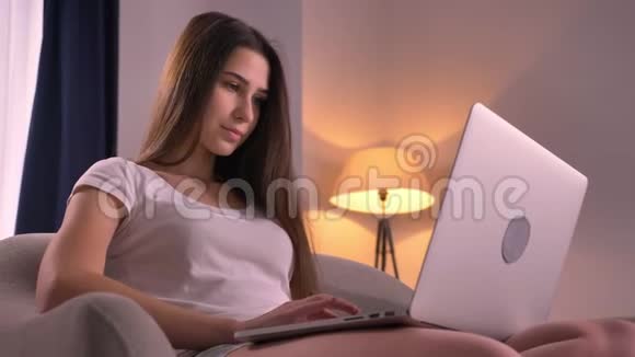 在室内舒适的家中年轻漂亮的少女在笔记本电脑上滚动的特写肖像视频的预览图