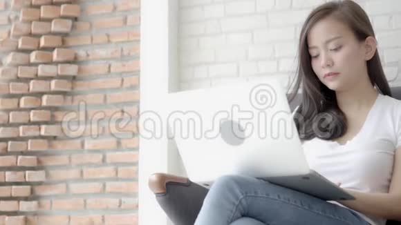 美丽的肖像亚洲年轻女子兴奋和高兴的成功与笔记本电脑沙发水泥背景视频的预览图
