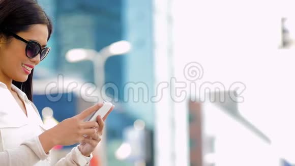 戴墨镜的亚洲女人在城里用智能手机视频的预览图