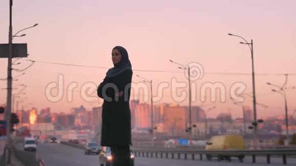 后景照片年轻迷人的穆斯林戴着头巾站在路边转向镜头与城市的城市视频的预览图