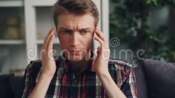 不高兴的年轻人正遭受着剧烈的头痛在家中触摸他的头部按摩太阳穴疼痛视频的预览图