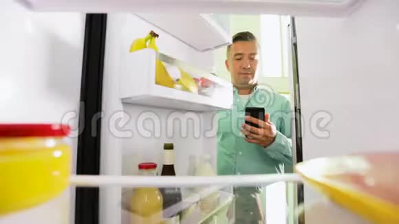 有智能手机的人在冰箱里列食物清单视频的预览图