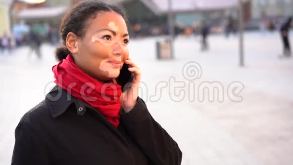 美丽的非洲女孩白癜风站在街上讲着手机微笑着视频的预览图