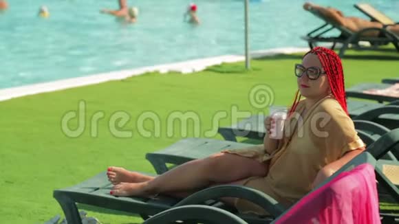 一个女人坐在泳池边的躺椅上喝奶昔视频的预览图