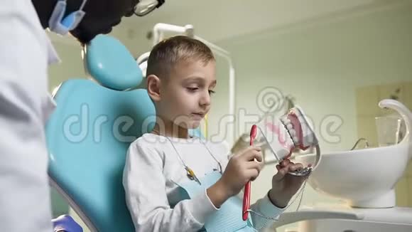 可爱的小男孩在牙医的监督下刷牙的塑料模型视频的预览图