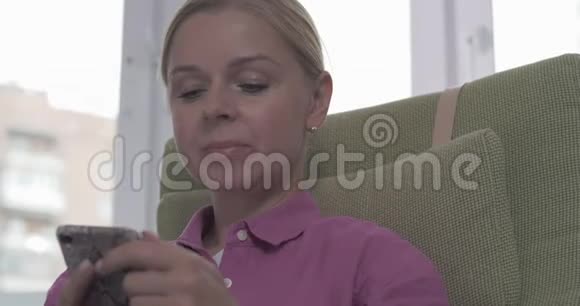 一位年轻的金发女子在智能手机上发短信时面带微笑视频的预览图