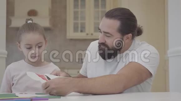 大胡子爸爸和一个漂亮的小女儿在一天假的时候坐在一张桌子上画着焰火帕斯蒂父亲和视频的预览图