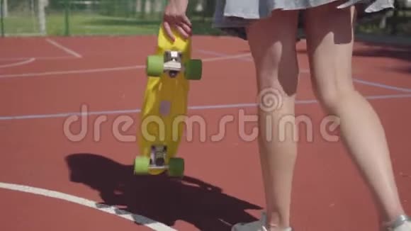 腿的女人穿着裙子带着黄色的滑板在篮球场上行走女式双腿运动鞋女式黄骑视频的预览图
