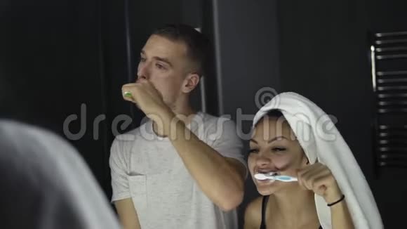 年轻的情侣在室内刷牙时照镜子女士头上戴着浴巾视频的预览图