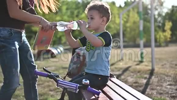 小男孩喝水坐在操场的长凳上生活方式视频没有稳定视频的预览图