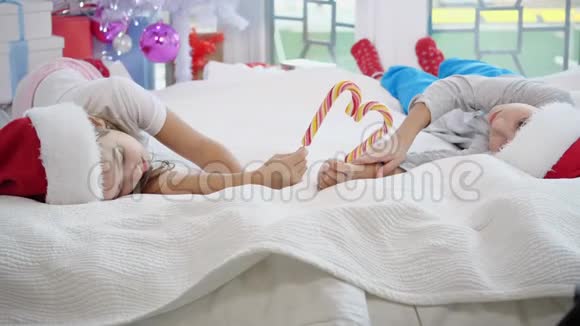 可爱的白种人孩子们享受圣诞节的早晨在床上玩耍用糖果罐头做心脏视频的预览图