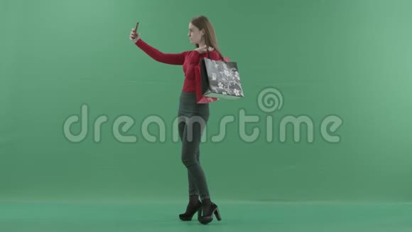 漂亮的女人穿着休闲服拿着购物袋在手机上自拍她站着视频的预览图