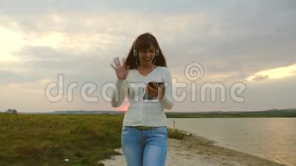 快乐女孩在线视频会议在夏天在公园湖边戴着耳机的漂亮女孩在海滩上视频的预览图