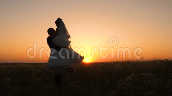 情人新娘穿着白色礼服新郎在夏天的夕阳下在田野里跳舞年轻的已婚夫妇亲吻拥抱视频的预览图
