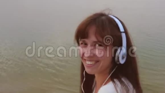 戴着耳机的快乐女孩在海滩散步时露出舌头和微笑视频的预览图