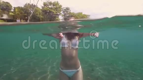 漂亮的女人在绿松石海水中游泳并寻找相机的水线视图一个棕色头发的女人在游泳视频的预览图