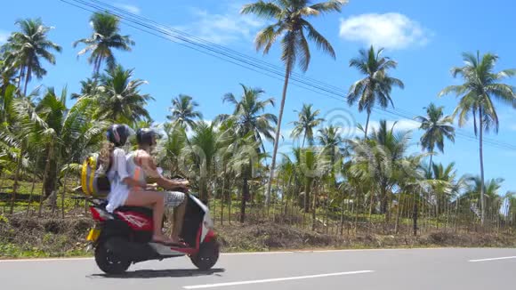 在热带国家一对年轻夫妇骑着一辆摩托车沿着沥青路行驶夏季骑脚踏车的背包客视频的预览图