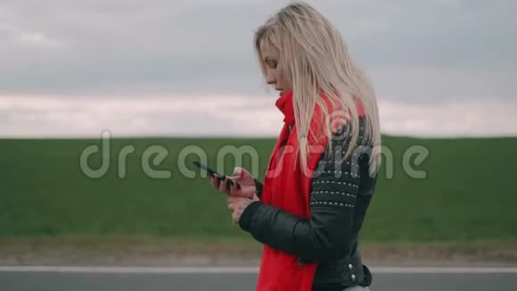 金发女人走在路上用智能手机戴着红领巾的女孩看着电话视频的预览图