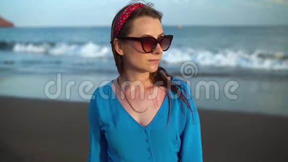 一个女人穿着漂亮的蓝色裙子在黑色火山海滩上的肖像慢动作视频的预览图