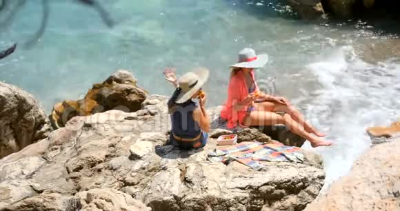 年轻漂亮的女人穿着泳衣在海边的岩石上做掩护视频的预览图