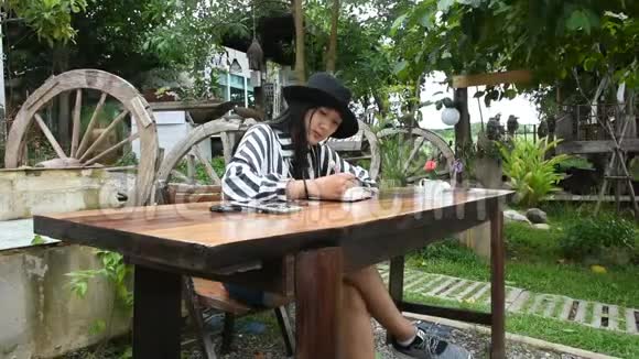 旅行者泰国女人坐在书上写纸条在花园里回忆视频的预览图
