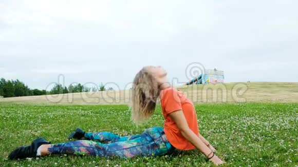 女人伸展她的背部弯曲躺在草地上女孩在城市公园的自然训练视频的预览图