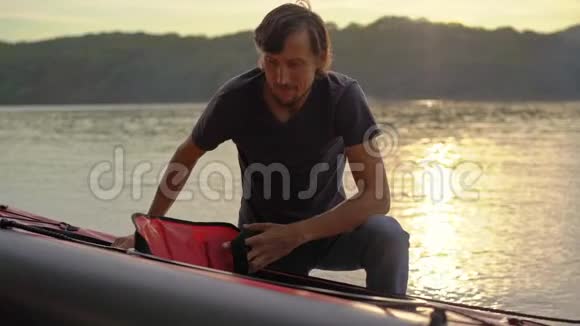 年轻人给他的皮艇充气准备在湖中划水慢镜头视频的预览图