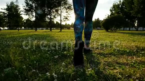 运动的女人穿着紧身衣和运动鞋在日落时分穿过草地视频的预览图