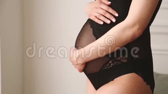 穿着黑色紧身衣的孕妇抚摸着她的腹部靠近白色的墙壁视频的预览图
