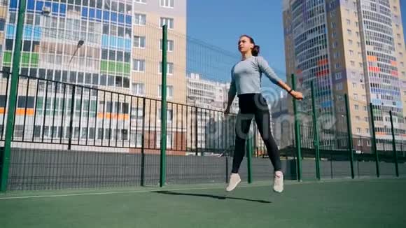 那个女孩在街道上的一个围栏地区参加体育活动街头健身操蹲着跳起来视频的预览图