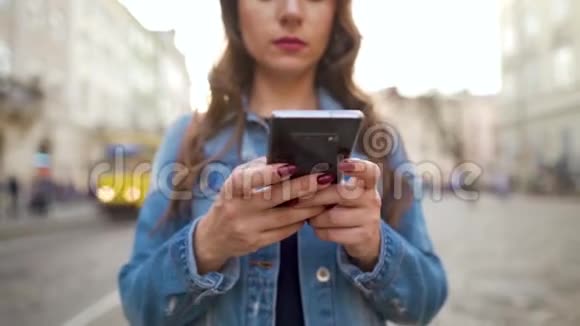 日落时分女人用智能手机走在老街上黄色有轨电车在后台交流社会视频的预览图