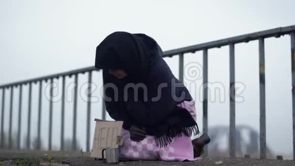 成年无家可归的妇女坐在桥上天气寒冷多风灰色要求施舍帮助和咳嗽视频的预览图