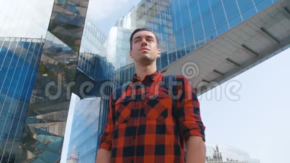 穿着格子衬衫背着背包环顾城市的旅游者大玻璃城市建筑背景视频的预览图