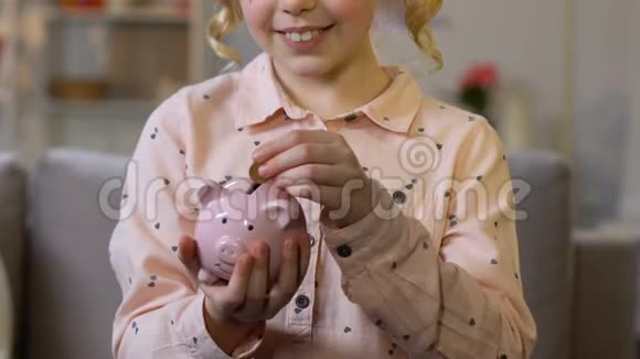 小女孩把硬币放进储蓄罐为孩子的梦想存钱特写镜头视频的预览图