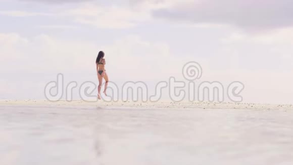穿着沙滩比基尼的年轻女子在白沙滩上跳来跳去快乐的女人在沙滩上享受夏日视频的预览图