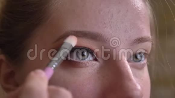 年轻的白人女化妆师在令人惊叹的棕色眉毛下涂上白色眼珠的特写肖像视频的预览图
