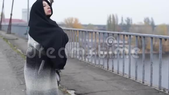 成年妇女在寒冷多风的灰色天气中穿过大桥停下来戴着围巾视频的预览图