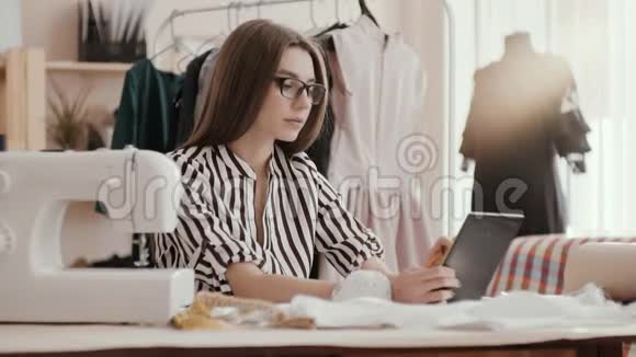 裁缝时装设计师在平板电脑上打字她的手在桌子上女孩被一个人体模型包围着视频的预览图