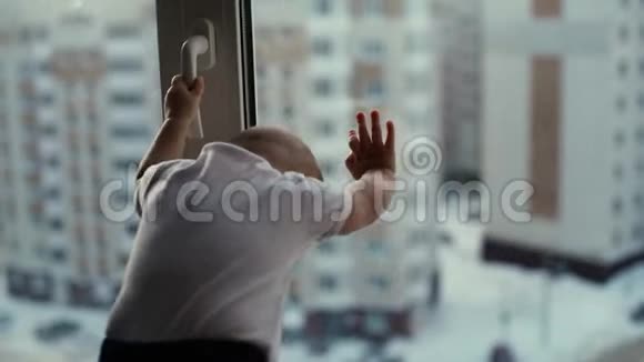 可爱的婴儿站在窗台上看着城市视频的预览图