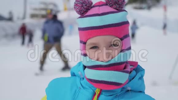 活跃的女孩戴着一顶滑稽的帽子微笑着看着冬天度假村的相机视频的预览图