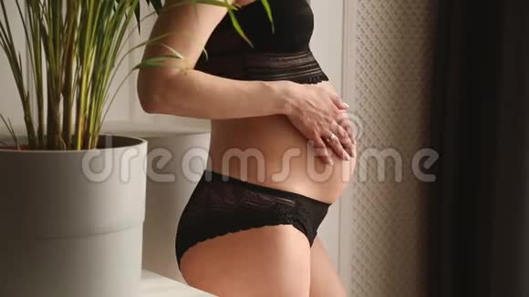 穿着黑色内衣的孕妇抚摸着窗户旁边的腹部视频的预览图