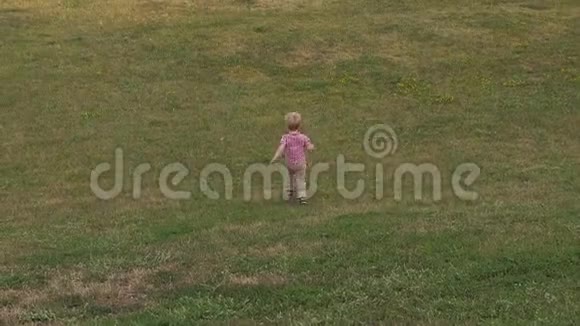 一个小男孩跑在公园的绿草上他跑下山视频的预览图
