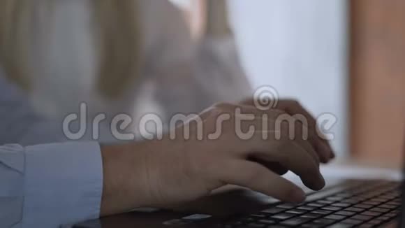 特写镜头男人手主动快速地打字在笔记本电脑的键盘上背景中的女性有助于指出视频的预览图