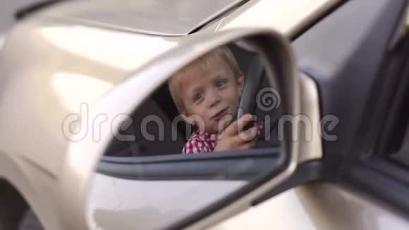 一个坐在汽车轮子后面的小男孩的车镜里的倒影视频的预览图