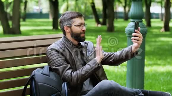 英俊的胡子男笑着视频电话在公园视频的预览图