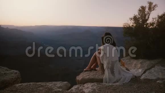 慢镜头电影拍摄快乐的年轻女子与头发吹在风坐在令人惊叹的日落大峡谷视频的预览图