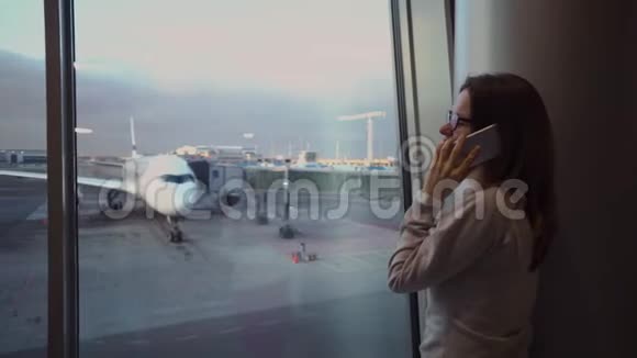 一个年轻漂亮的女孩在机场候机楼的飞机背景下打电话视频的预览图