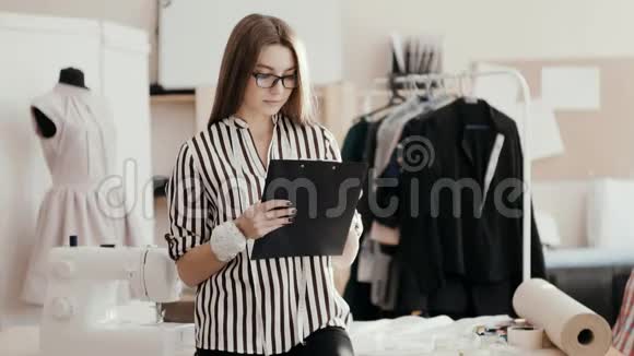 女时装设计师在平板电脑上画了一幅裙子的草图看着相机微笑着年轻的商务小姐视频的预览图