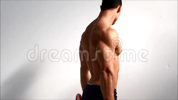 年轻的健美运动员训练陷阱和肩膀上的哑铃从后面看视频的预览图